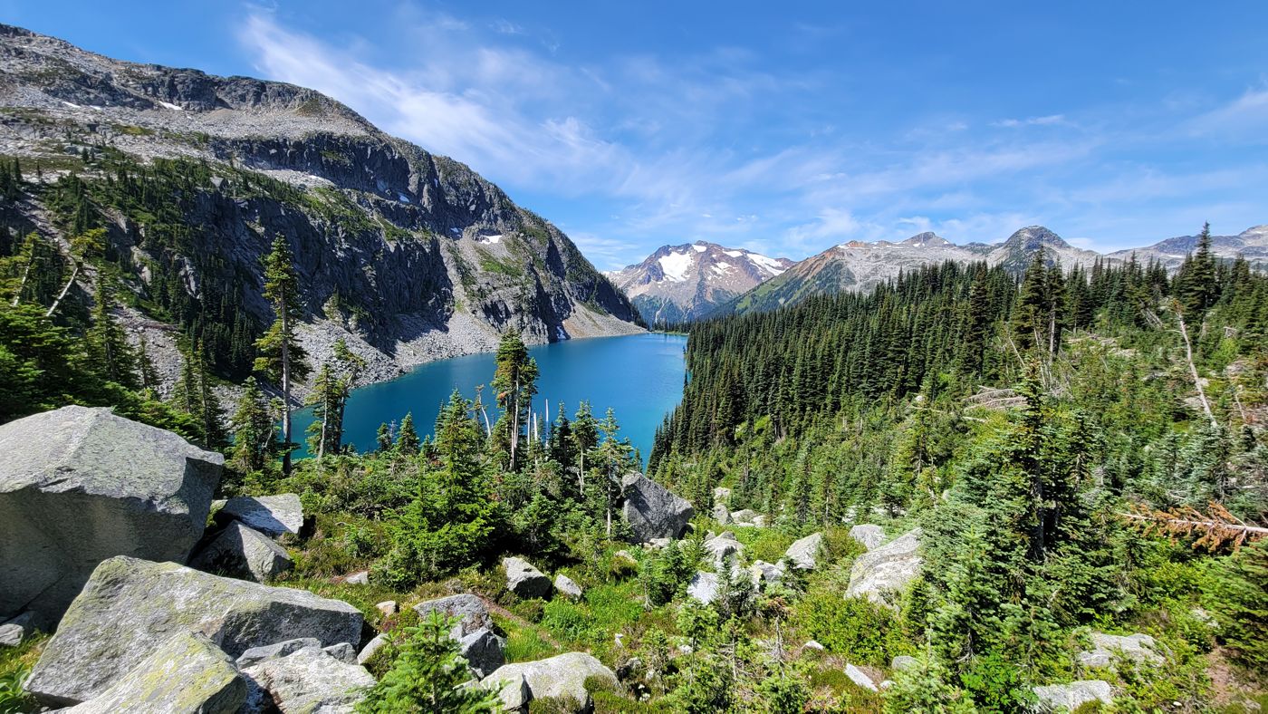Turquoise alpine lake below forested slopes and snowy peaks